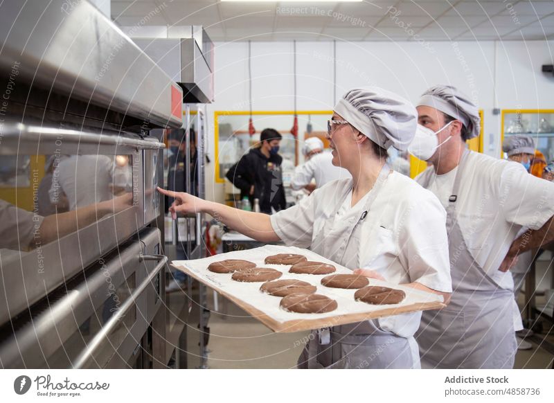 Frau mit rohem Brot beim Einschalten des Ofens Bäckerei Teigwaren lernen Schule antörnen Menschen elektrisch Küche Industrie backen Rezept vorbereiten