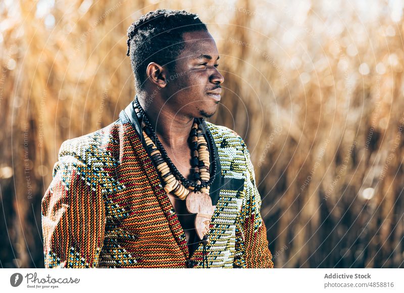 Afrikanischer Mann in perlenbesetzter Jacke in der Nähe eines Feldes Tradition Outfit Stil Mode Ornament Halskette authentisch männlich schwarz ethnisch Wulst