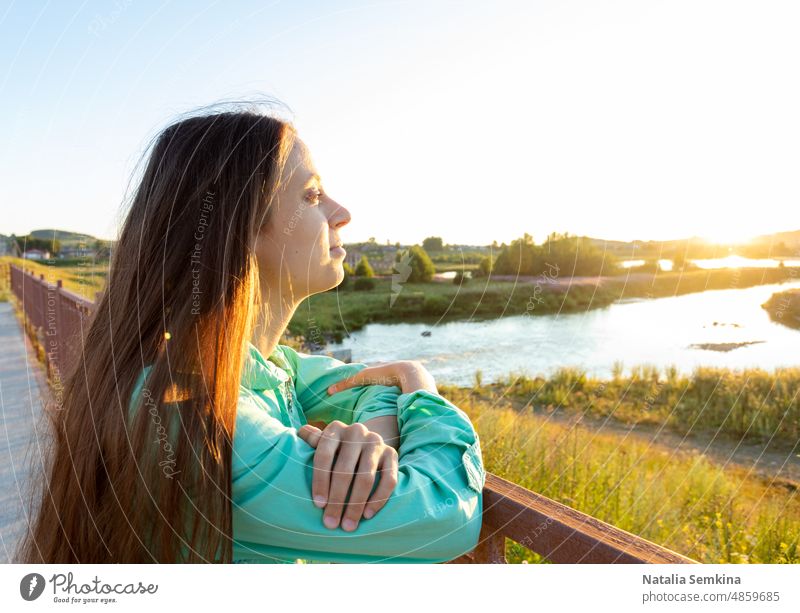 Junges Mädchen mit offenen langen Haaren bewundert den Sonnenuntergang am Fluss an einem Sommerabend auf dem Lande. junges Mädchen verträumt goldene Stunde