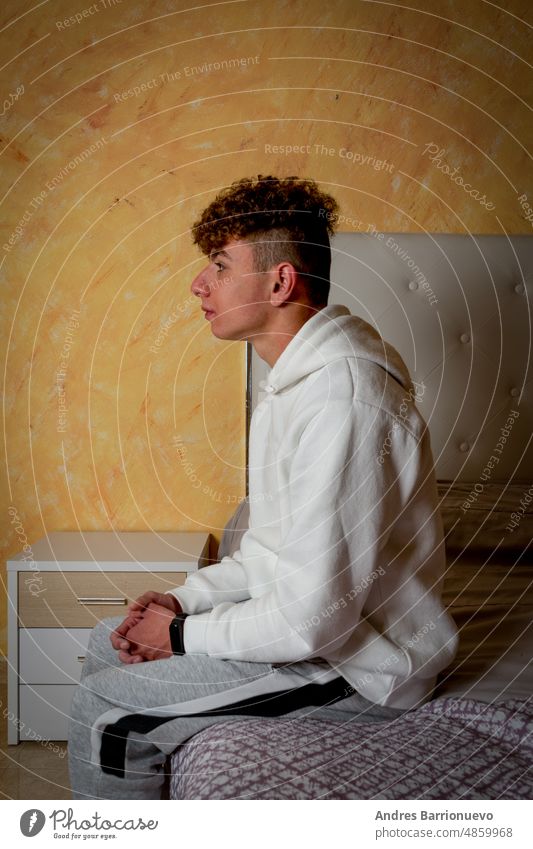 Junger Mann mit lockigem Haar sitzt auf dem Bett in seinem Zimmer mit traurigen und depressiven Haltung, Einsamkeit Konzept. Schlafzimmer jung gestresst