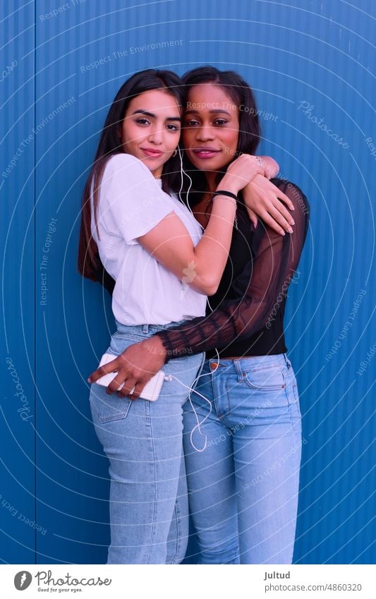 Zwei Freunde umarmen sich vor einer blauen Wand. Mädchen Ethnizität Spanien jung Frau Zwanziger Jahre trendy Gebäudeaußenseite Freundin Freundschaft