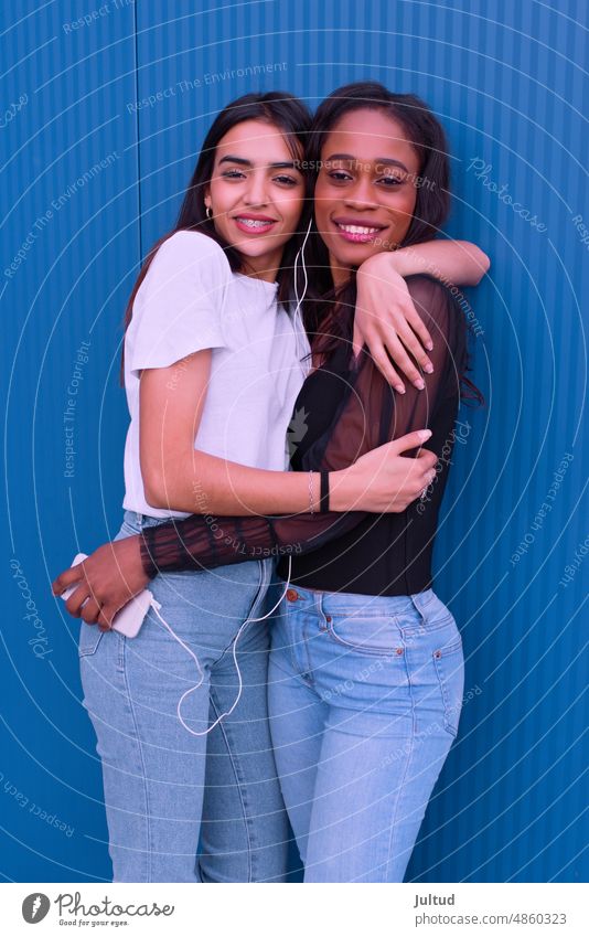 Zwei Freunde umarmen sich vor einer blauen Wand. Mädchen Ethnizität Spanien jung Frau Zwanziger Jahre trendy Gebäudeaußenseite Freundin Freundschaft