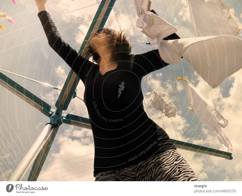 Eine Frau hängt Wäsche auf eine Leine, Wäschespinne Wäscheleine Wäsche waschen Haushalt Waschtag aufhängen Häusliches Leben Himmel Wolken Froschperspektive