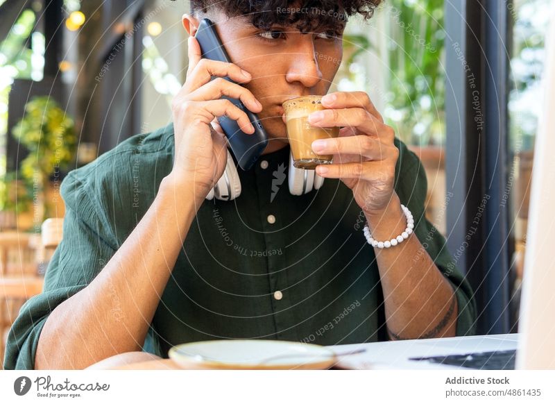 Junger Mann mit Laptop und Smartphone in einem Café freiberuflich trinken Kaffee Mobile Arbeit abgelegen modern Netbook Gerät Kopfhörer ethnisch lässig männlich