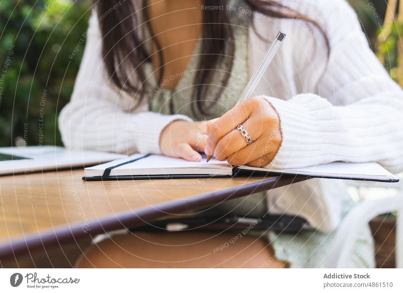 Anonyme selbständige Frau, die in einem Café im Freien in ein Notizbuch schreibt zur Kenntnis nehmen Notebook schreiben freiberuflich Plan Zeitplan Terrasse