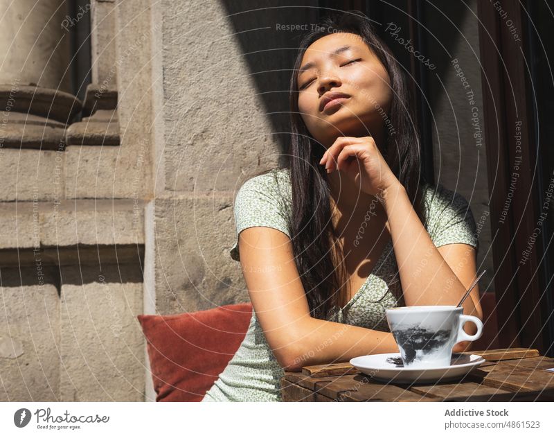 Charmante asiatische Frau am Tisch mit Kaffee im Straßencafé Café Getränk Terrasse genießen verträumt Augen geschlossen Sommer Heißgetränk feminin trinken