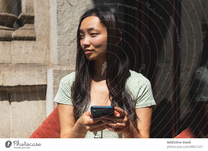 Asiatische Frau, die in einem Straßencafé auf ihrem Smartphone surft Browsen Surfen online Café Sommer Terrasse Textnachricht soziale Netzwerke Internet