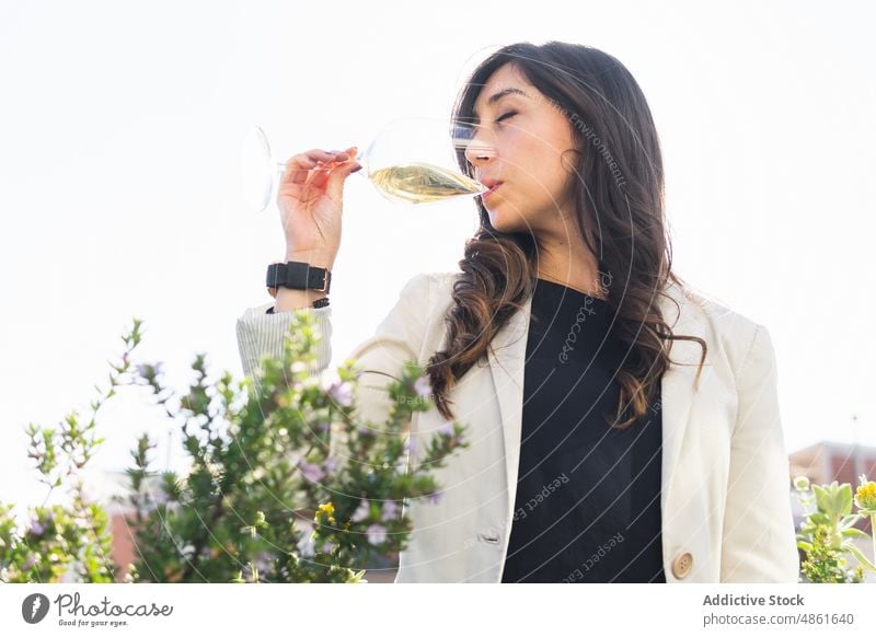 Weiblicher Sommelier riecht an Wein auf der Terrasse Frau riechen degustieren Sitzung Sommer trinken Weißwein tagsüber Wochenende Erwachsener brünett hispanisch