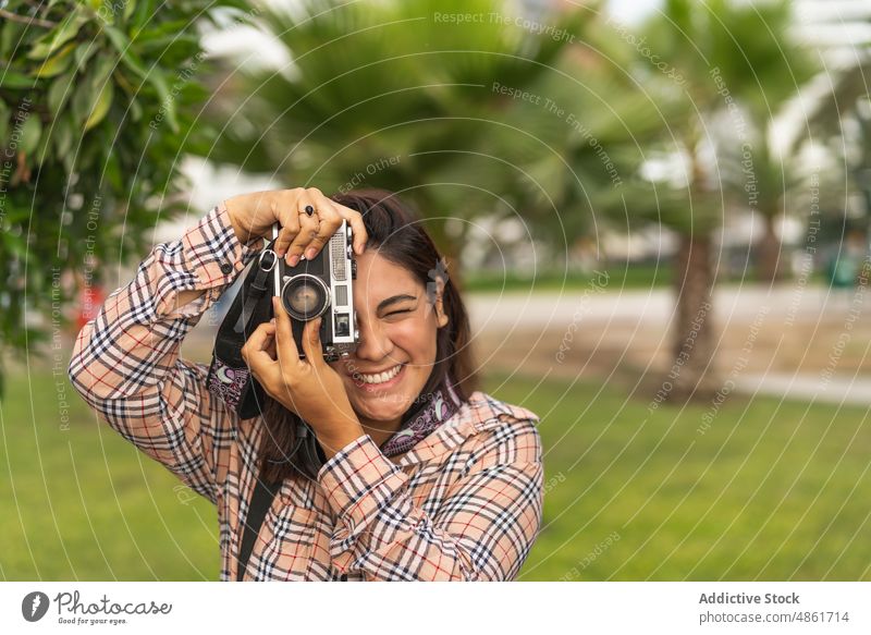 Positive ethnische Frau, die mit einer Retro-Kamera im Stadtpark fotografiert fotografieren Fotoapparat altehrwürdig Tourist Lächeln heiter Fotografie tropisch