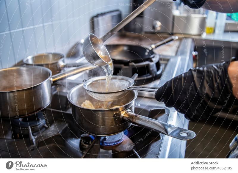 Koch trennt Wasser von Reis mit Hilfe eines Siebs in der Küche Küchenchef Trennen wirtschaftlich Gießen Kochtopf Herd Utensil industriell Essen zubereiten
