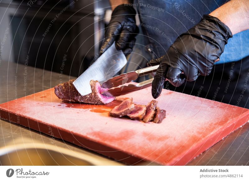 Chefkoch schneidet Grillsteak im Küchenrestaurant Küchenchef Hand Schneiden Grillrost Steak Messer Schneidebrett Restaurant Zange Handschuh Beteiligung Fleisch