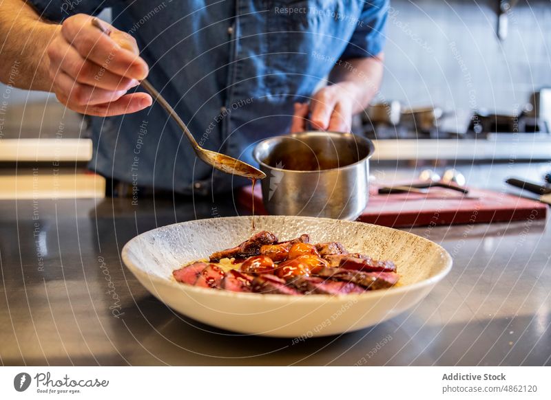 Anonymer Chefkoch gießt Soße auf Rindfleisch in einer Schüssel im Restaurant Küchenchef Gießen Saucen Schalen & Schüsseln wirtschaftlich Löffel Speise