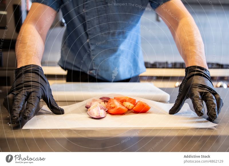 Anonymer Koch mit geschnittener Zwiebel und Tomate auf Backpapier Küchenchef Scheibe Hand Handschuh Restaurant Essen zubereiten Lebensmittel Schneidebrett