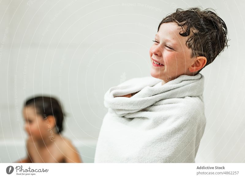 Positiver Junge in weißes Handtuch gewickelt nach dem Baden Lächeln Kind Badewanne Hygiene Verfahren Porträt Zahnfarbenes Lächeln Glück positiv heiter Freude