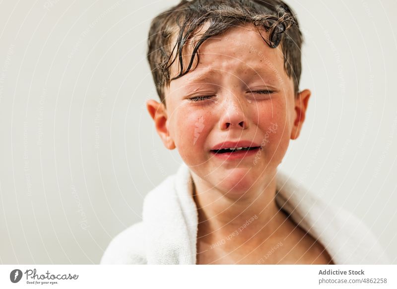 Trauriger Junge mit Tränen im Gesicht, eingewickelt in ein weißes Handtuch traurig verärgert Kind Augen geschlossen nasses Haar weinen Porträt Problematik