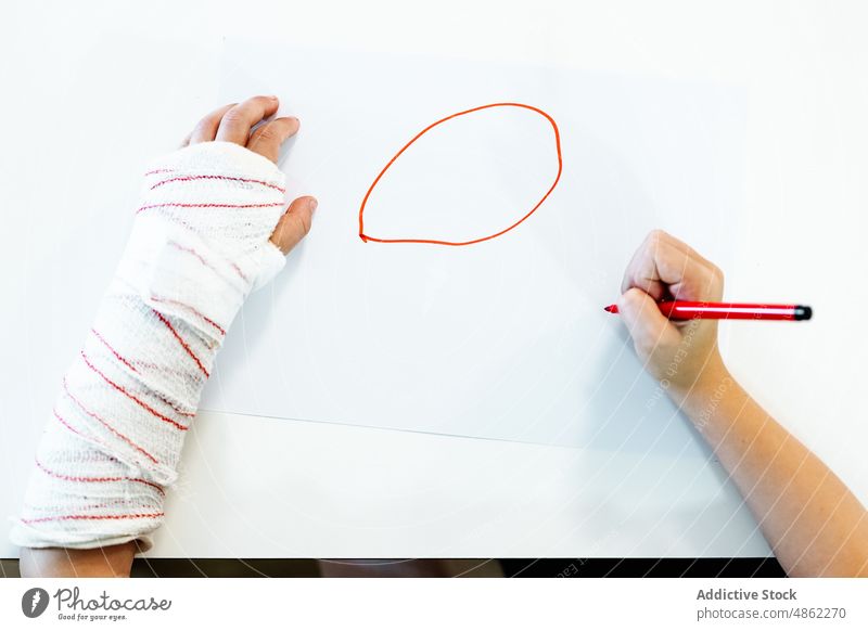 Anonymer Junge mit gebrochenem Arm Zeichnung zeichnen Bild Markierung kreativ Arme Hobby heimwärts Tisch Kind sitzen Kunst Schreibstift Talent kreisen Hände