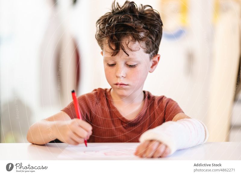 Junge mit gebrochenem Arm Zeichnung zeichnen Bild Markierung kreativ Arme Hobby heimwärts Tisch Kind Wochenende sitzen Kunst Schreibstift Talent Kindheit