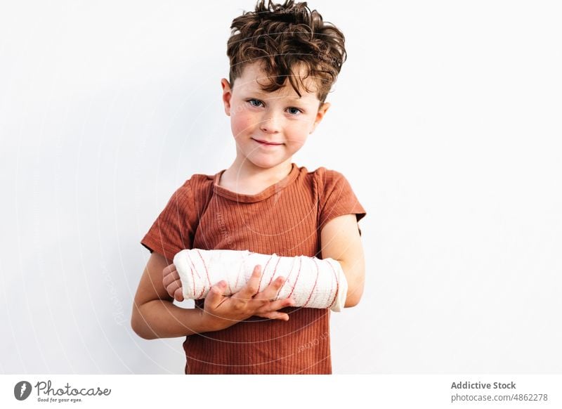 Niedlicher Junge mit gebrochenem Arm in Gipsbinde Lächeln bandagieren Verletzung verputzen geduldig Schmerz wehtun Glück Problematik Kindheit behüten niedlich
