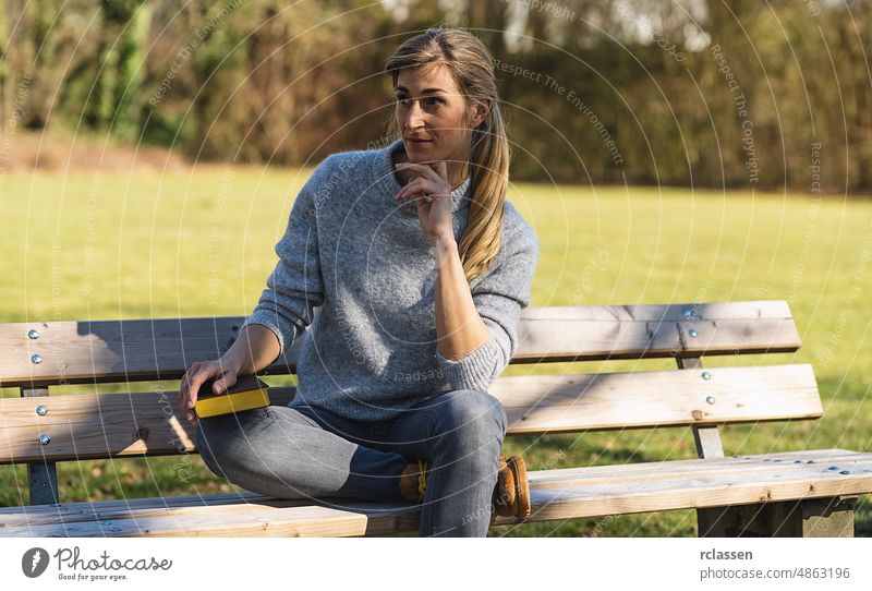 Nachdenkliche Frau sitzt im Park auf einer Bank. Studentin denkt mit einem Buch im Park Konzeptbild Mädchen Behaarung hübsch Baum attraktiv Denken Flirten