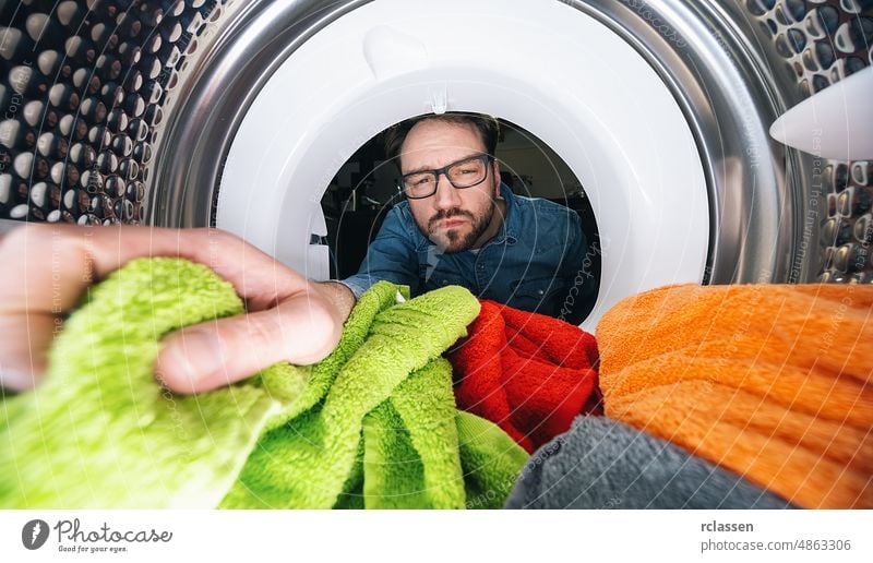 Mann mit Brille greift in eine Waschmaschine oder einen Trockner und wäscht Wäsche Ansicht von innen stürzen im Inneren Wäscherei Maschine erreichend