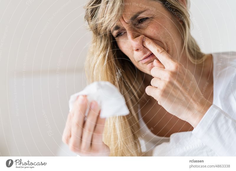 Kranke Frau bohrt in der Nase. Upset kranken europäischen Dame sitzt im Bett, bläst und pickt ihre Nase mit Papierserviette Gewebe. Erkältung und Grippe Konzept