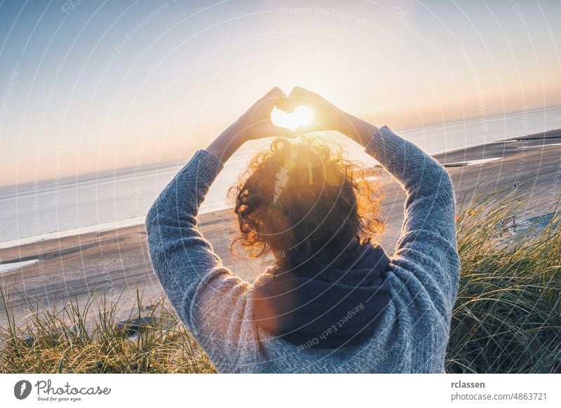 Mädchen hält eine Herzform mit Sonnenuntergangslicht am Strand Frau Hand Lifestyle reisen Liebe Harmonie Kräusel Konzept Sonnenlicht Morgendämmerung Symbol