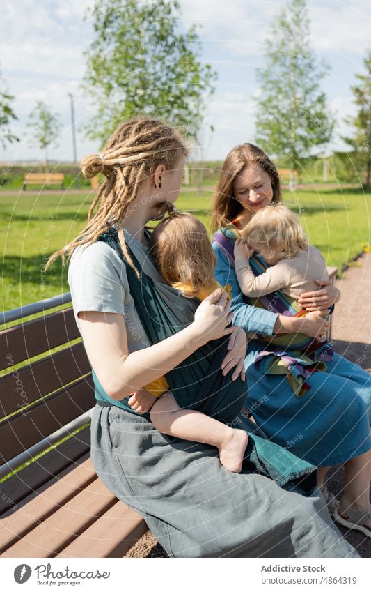 Mütter mit ihren Babys auf einer Bank im Park sitzend Mutter Sitzen sonnig Freund Babytragetuch Zusammensein Liebe Bonden Freizeit Lifestyle Lächeln Glück