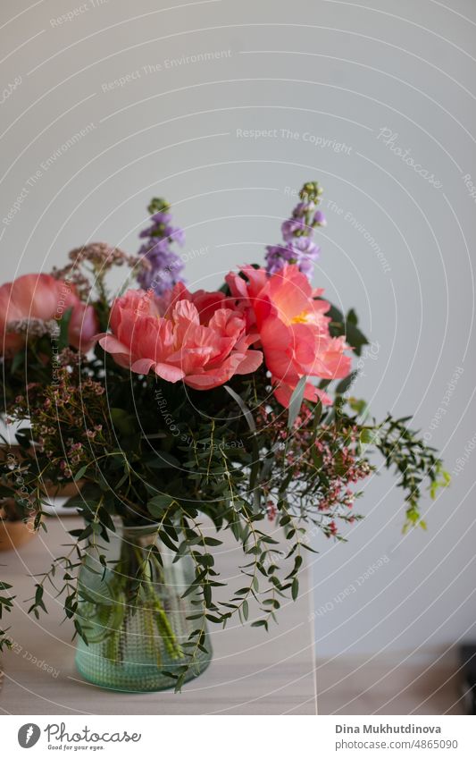 Schöne Bouquet mit rosa Korallen Pfingstrosen und Grüns in einer Vase auf Holztisch zu Hause. Heimdekoration mit Blumen. Dekoration zu Hause und Gemütlichkeit. Geschenk für einen Geburtstag, Jahrestag oder Muttertag. Romantische Geste.