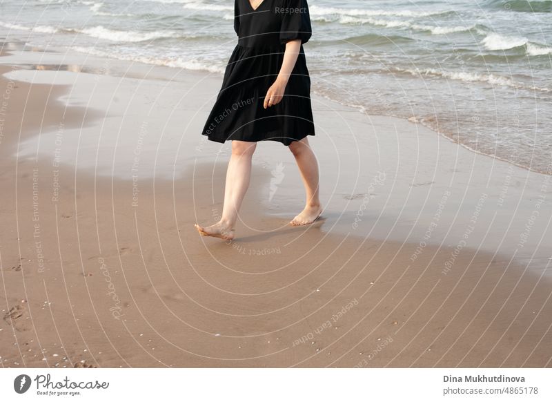 Barfuß Frau zu Fuß auf dem Sandstrand weg von den Wellen des Meeres. weiblichen Touristen im Urlaub und Reisen. Barfuß Füße auf Sand. Wellen des Meeres entlang der Küste. Frau zu Fuß entlang der Küste.