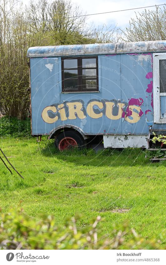 alter Zirkuswagen im Garten Sonnenlicht Kontrast Licht Textfreiraum unten Farbfoto Außenaufnahme blau Artist Aufschrift Buchstaben Einsamkeit außergewöhnlich