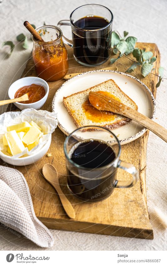 Zwei Gläser Kaffee, eine Brotscheibe, Butter und Marillen Marmelade auf einem Holz Serviertablett Frühstück Aprikose süß Espresso Lebensmittel lecker Ernährung