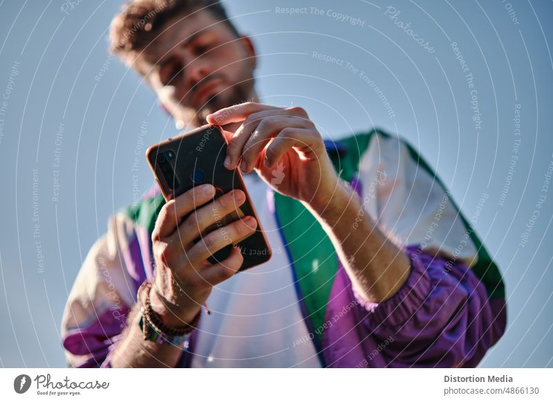 Junger Mann schaut von unten auf sein Mobiltelefon, Fokus auf das Telefon Erwachsener Anwendung Hintergrund Unschärfe-Effekt lässig Kaukasier heiter Mitteilung