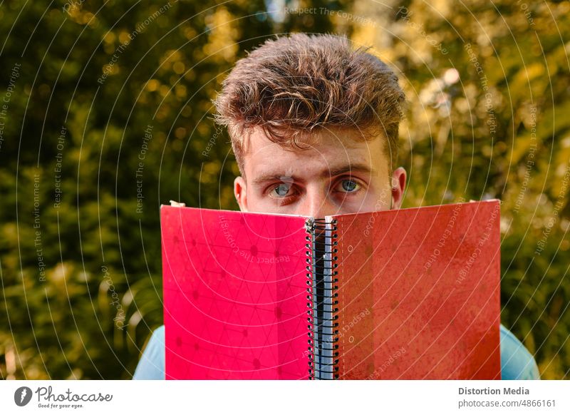 Blauäugiger Student, der vor Prüfungen Angst hat und sein Gesicht mit einem roten Notizbuch bedeckt Autodidakt Herbst schön Schönheit Kaukasier Kultur niedlich