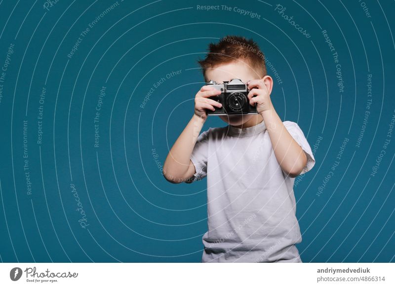 Kleiner Junge nimmt ein Bild mit einer Retro-Kamera. Kind Junge mit Vintage-Foto-Kamera isoliert auf blauem Hintergrund. Alte Technologie Konzept mit Kopie Raum. Kind lernt Fotografie