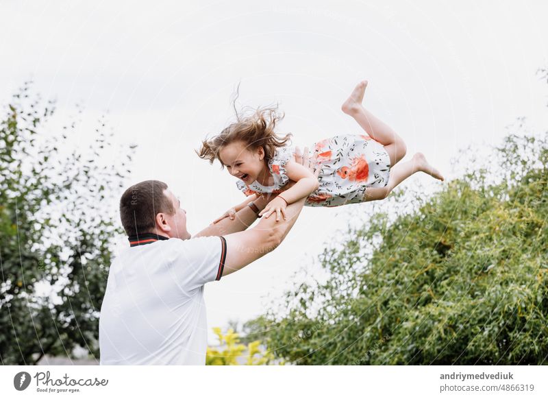 Junger Vater wirft sein Baby Tochter hoch in den Himmel im Park im Sommer Tag. Vatertag Glück Kindheit Freude wenig Papa Menschen Spaß Familie im Freien