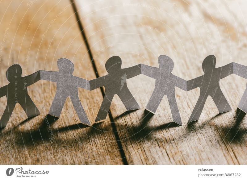 Papiermenschen, die sich an den Händen halten, auf einem Holztisch Menschen Team geschnitten anketten Link Zusammensein abstützen Freundschaft Unternehmen