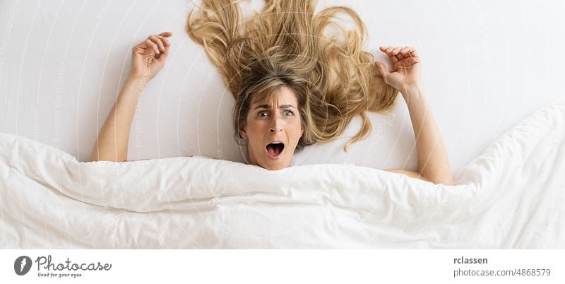 Draufsicht auf eine schöne Frau, die überrascht ist und mit offenem Mund schaut, während sie im Bett unter einer Decke liegt Top lustig Ansicht Sex Lügen wach