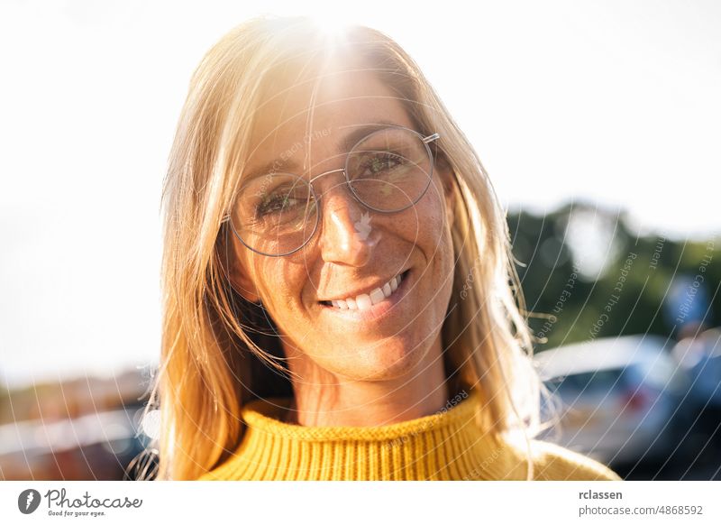 Porträt der schönen Frau lächelnd und Blick auf die Kamera mit Brille bei Sonnenuntergang. Outdoor-Porträt eines lächelnden Mädchens. Glücklich fröhliche Mädchen lachen in der Stadt mit gelben Pullover.