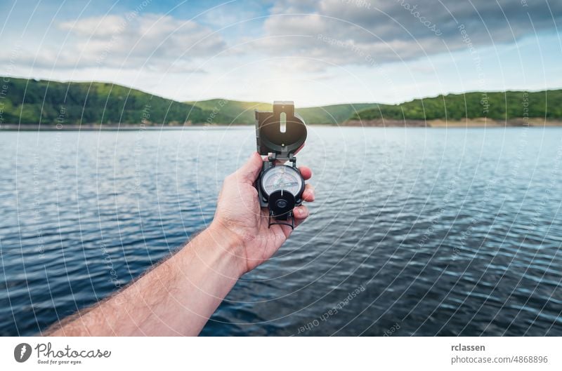 Reisender Mann sucht Richtung mit einem Kompass an einer Küste in der Nähe eines Sees in den Bergen. Point of view shot. Beteiligung pov Orientierung Hand