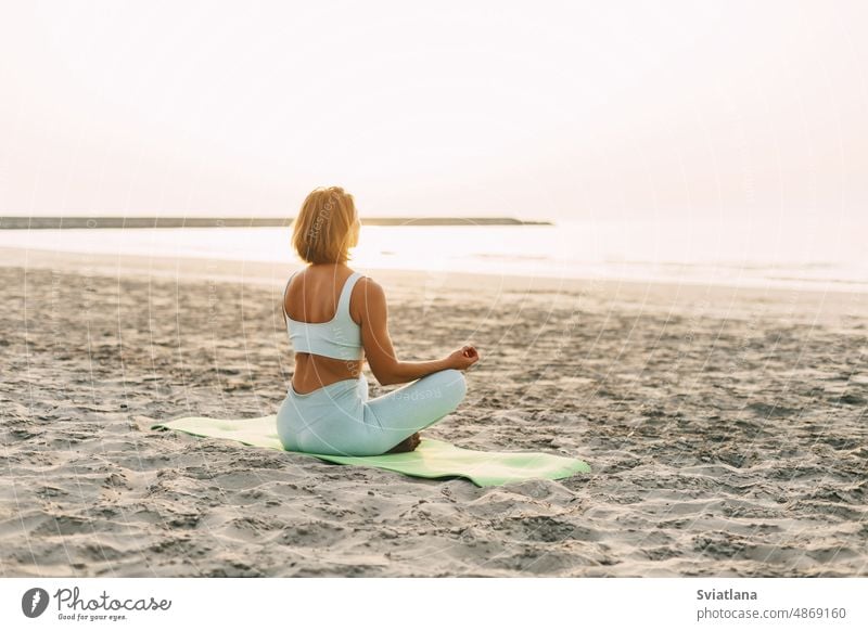 Junge Frau meditiert in Lotus-Pose am Strand in der Nähe des Meeres bei Sonnenuntergang im Sommer, Rückansicht Mädchen Yoga Fitness Lotos MEER jung Rückseite