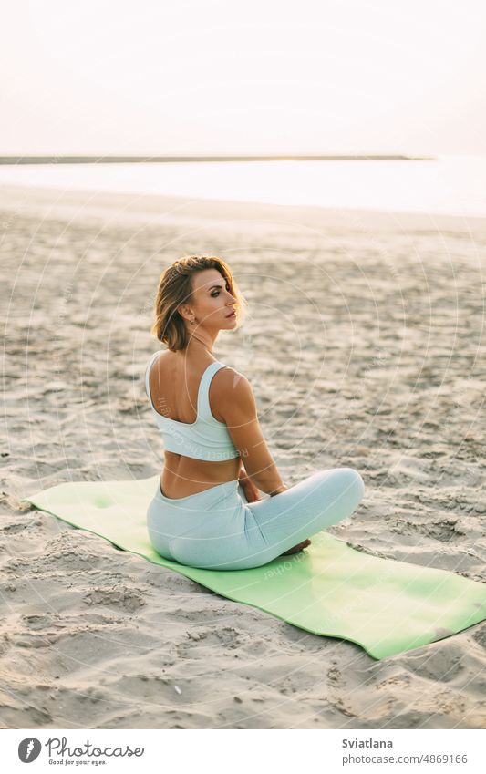 Ein schönes Mädchen sitzt am Meeresufer im Lotussitz und ruht sich nach Yoga- oder Fitnesskursen aus. Gesunder Lebensstil, Selbstfürsorge, Aktivität Strand Frau