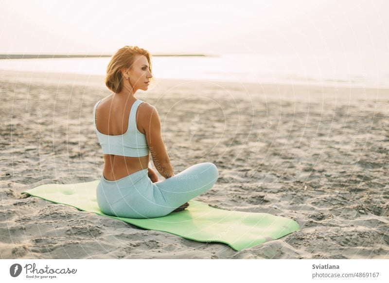 Ein schönes Mädchen sitzt am Meeresufer im Lotussitz und ruht sich nach Yoga- oder Fitnesskursen aus. Gesunder Lebensstil, Selbstfürsorge, Aktivität Strand Frau