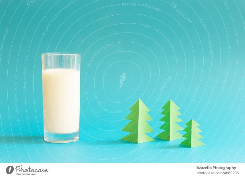 Glas Milch und grüner Origami-Wald auf blauem Hintergrund. melken Baum Pastell Stillleben Dorf Natur Minimalismus Schatten trinken Kuh Bauernhof natürlich