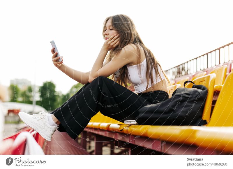 Ein junges Mädchen sitzt auf der Tribüne der Schule und schreibt in ihrer Freizeit eine Nachricht auf ihrem Handy Telefon Schulmädchen tagsüber Smartphone
