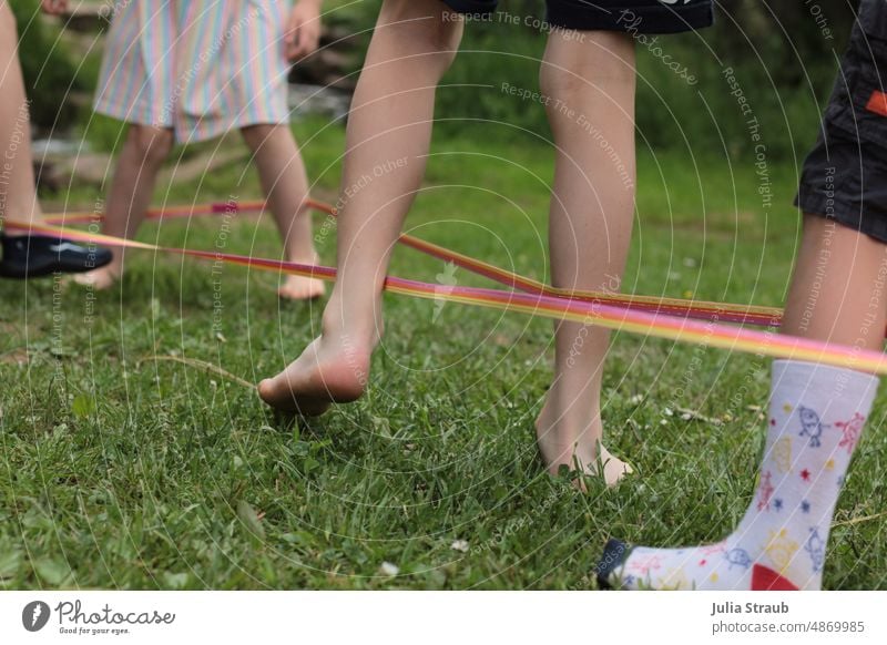 Kinder spielen draussen auf der Wiese gemeinsam Hüpfgummi Gummitwist Kinderspiel Kindergarten hüpfen Kindheit Barfuß Socken Sommer grün Natur Zusammensein