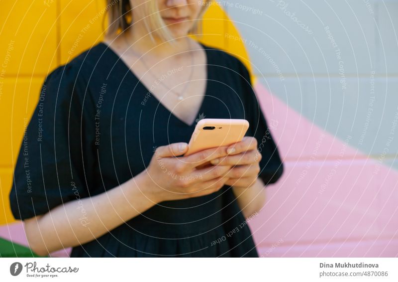 Junge Frau mit Handy steht in der Nähe von bunten Wand nehmen Selfie oder Video-Chat auf dem Smartphone. Bildschirmzeit. Lebensstil mit Technologie. Junge Remote-Arbeiter Mitarbeiter in modernen Büroraum.