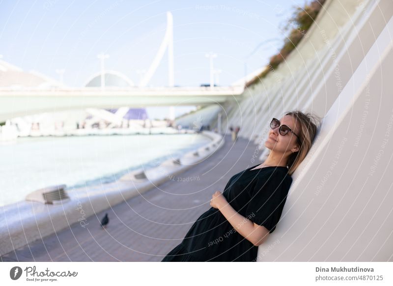 Junge weibliche Tourist in Sonnenbrille bewundern die Aussicht auf die europäische Stadt am sonnigen Tag. Frau Sightseeing im Sommer im Urlaub in Ort mit moderner Architektur im Hintergrund. Hitzewelle in Europa, die Touristen und Reisende betrifft.