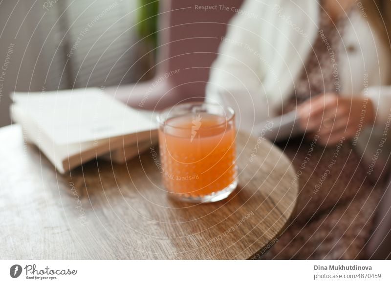 Ein Cocktail von Pfirsich orange Farbe auf dem Tisch im Café, Restaurant oder zu Hause auf Holztisch. Lifestyle-Foto von Frau lesen Anzeige trinken einen erfrischenden Saft trinken.