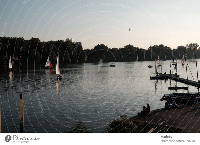 Bunte Segelboote und Jollen sowie ein Heißluftballon im Licht der Abendsonne auf dem Aasee in Münster in Westfalen im Münsterland Wochenende Abendstimmung ufer