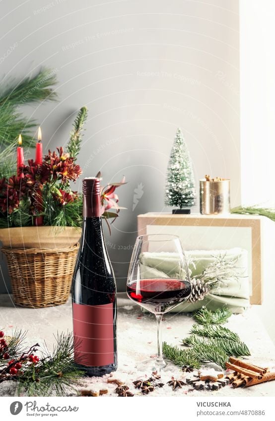 Rotweinflasche mit Weinglas und Tannengrün am Tisch mit Weihnachtsdekoration und Wintergewürzen Stillleben Flasche Wand Hintergrund Vorderansicht Textfreiraum